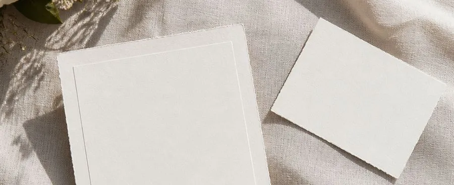 A formal wedding invitation lying apart from a separate enclosure card and a laptop edge