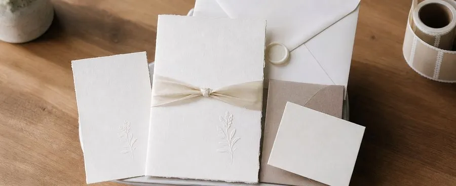 A wedding invitation suite on a kitchen scale beside a roll of postage stamps.