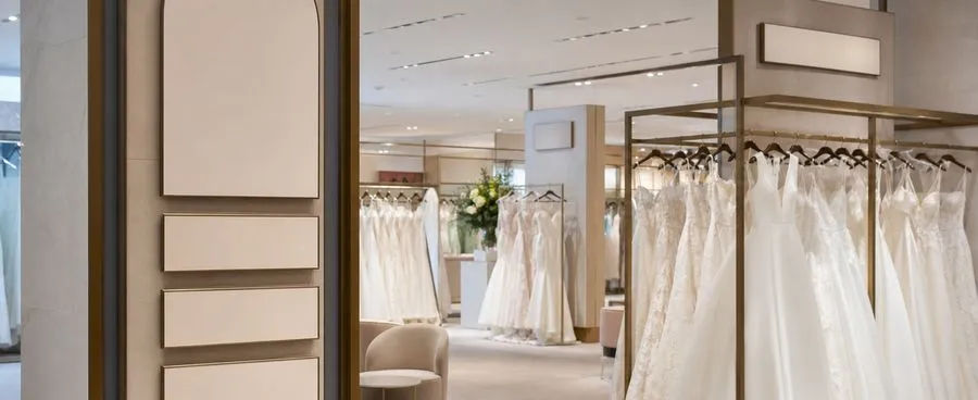 A department-store bridal section with designer-labeled gown racks under soft lighting
