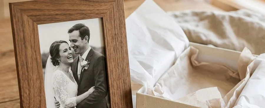 Personalized engraved wood picture frame with two names and a wedding date beside an open gift box.