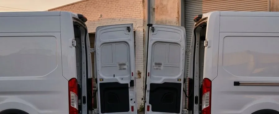 Two unmarked delivery vans facing each other across an empty loading bay, a single wrapped bouquet resting on the pavement between them.